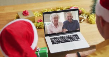 Noel Baba şapkalı beyaz bir baba ve oğul. Ekranda bir çiftle yılbaşı görüntüsü için dizüstü bilgisayar kullanıyorlar. Noel, şenlik ve iletişim teknolojisi.