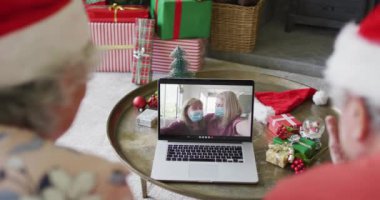 Kafkasyalı yaşlı çift, ekranda aileleriyle yılbaşı görüntüsü için dizüstü bilgisayar kullanıyor. Covid 19 salgını sırasında Noel, şenlik ve iletişim teknolojisi.