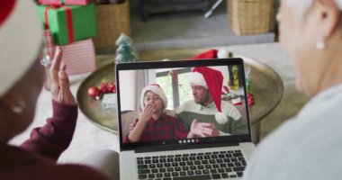 Farklı son sınıf kız arkadaşları, ekranda mutlu bir aileyle yılbaşı videosu için dizüstü bilgisayar kullanıyor. Noel, şenlik ve iletişim teknolojisi.