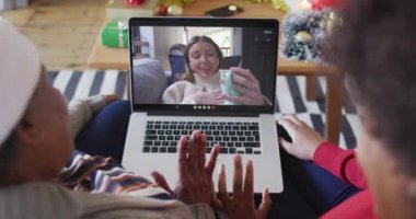 Afrika kökenli Amerikalı anne ve kız. Ekrandaki kadınla yılbaşı videosu için dizüstü bilgisayar kullanıyorlar. Noel, şenlik ve iletişim teknolojisi.