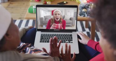 Afrika kökenli Amerikalı anne ve kız. Ekrandaki kadınla yılbaşı videosu için dizüstü bilgisayar kullanıyorlar. Noel, şenlik ve iletişim teknolojisi.