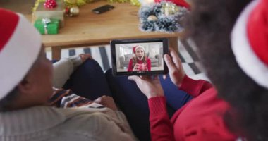 Afrika kökenli Amerikalı anne ve kız. Ekranda bir kadınla Noel videosu için tablet kullanıyorlar. Noel, şenlik ve iletişim teknolojisi.