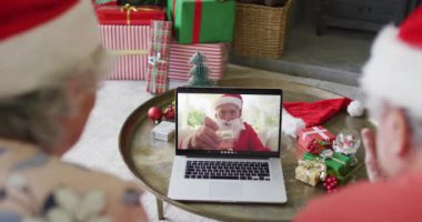 Üst düzey Kafkasyalı çift Noel 'de ekranda mutlu noel baba videosu için dizüstü bilgisayar kullanıyor. Noel, şenlik ve iletişim teknolojisi.