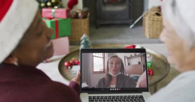 Farklı son sınıf kız arkadaşları, ekranda mutlu bir kadınla yılbaşı görüntüsü için dizüstü bilgisayar kullanıyor. Noel, şenlik ve iletişim teknolojisi.