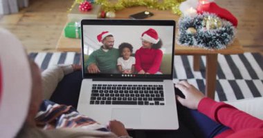 Afrika kökenli Amerikalı anne ve kız, ekranda ailesiyle birlikte yılbaşı görüntülü konuşma için dizüstü bilgisayar kullanıyorlar. Noel, şenlik ve iletişim teknolojisi.