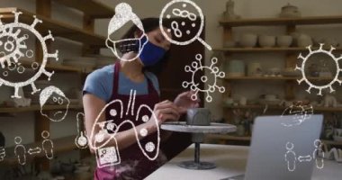 Yüz maskesi takan bir kadının çömlek atölyesinde çalışması üzerine covid 19 ikonu. küresel covid 19 salgın konsepti dijital olarak oluşturulmuş video.