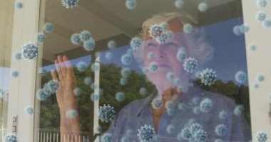 Virüs hücrelerinin evde gülümseyen yaşlı beyaz bir kadın üzerinde canlandırılması. Dijital olarak üretilen video pandemik konsept covid 19 sırasında evde yalnız zaman geçirmek.