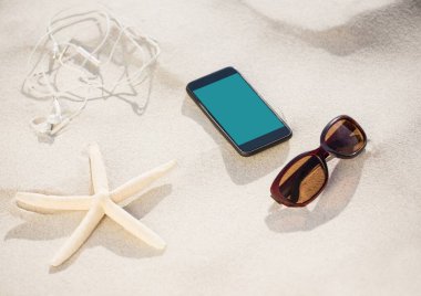 Akıllı telefon, güneş gözlüğü, kulaklık ve sahilin kumsalında fotokopi alanı olan yıldız balığı. Yaz tatili ve seyahat konsepti