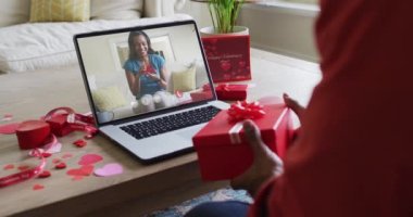 Afro-Amerikan kadının hediyesini açması ve sevgililer günü videosunu dizüstü bilgisayarına kaydetmesi. Sevgililer Günü kutlaması, romantizm ve iletişim teknolojisi.