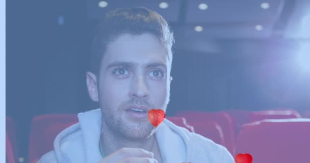 映画の中でポップコーンを食べる白人男性の上にハートアイコンのアニメーション ポップコーンの日とお祝いのコンセプトデジタル生成ビデオ — ストック動画