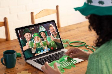 Evde dizüstü bilgisayarında telefon görüşmesi yaparken elinde yonca gözlüğü olan beyaz bir kadın. Aziz Patrick 'in kutlama konsepti