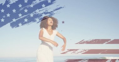 Sahilde elini kaldıran Afro-Amerikan kadının Amerikan bayrağının animasyonu. Vatanseverlik ve kutlama konsepti dijital olarak oluşturulmuş video.