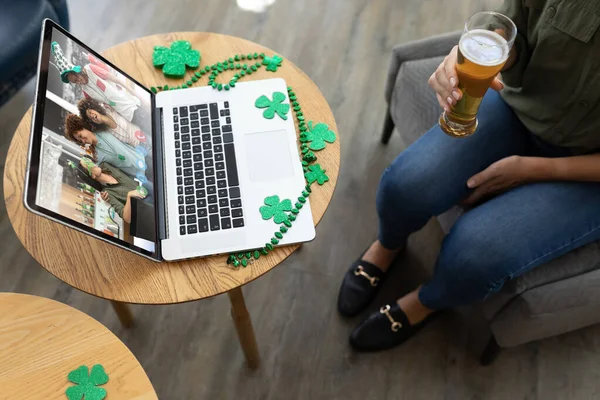 Mid section of woman holding a beer glass while having a video conference on laptop at a bar. st patricks celebration concept