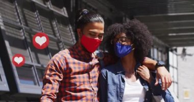 Yüz maskesi takan ve teknolojiyi kullanan kadın ve erkeğin üzerine düşen ikonların videosu. covid 19 salgın konsepti sırasında dijital olarak üretilen küresel ağlar, iş ve bağlantılar.