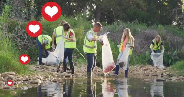 田舎の川でゴミを拾う多様なグループの上に赤い心のアニメーション 環境保全ボランティアの月デジタル生成ビデオ — ストック動画
