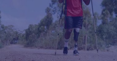 Doğada yürüyen protez bacaklı ve koltuk değnekli melez bir adamın üzerine ışık videosu. Ulusal yürüyüş günü, engellilik, aktif yaşam tarzı dijital olarak oluşturulmuş video.