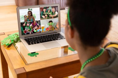 Karışık ırkçı kadın evdeki laptopta Patrick 'in günü için arkadaşlarına video görüşmesi yapıyor. Karantina süresince evde tecrit edilmiş İrlandalı koruyucu azizlerin gününü kutluyoruz..