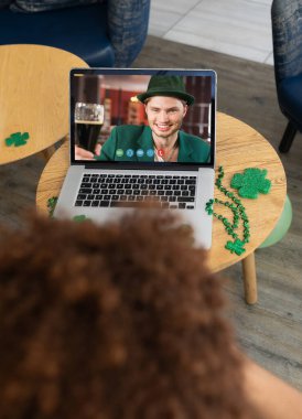 Bardaki adam dizüstü bilgisayarda gülümseyen beyaz erkek arkadaşına Aziz Patrick Günü videosu çekiyor. İrlanda Koruyucu Azizler Günü 'nün kutlaması sırasında.