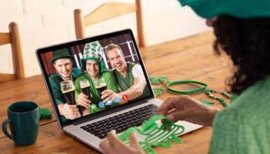 Kostüm giymiş melez bir kadın dizüstü bilgisayardaki erkek arkadaşlarına Aziz Patrick Günü videosu çekiyor. Karantina süresince evde tecrit edilmiş İrlandalı koruyucu azizlerin gününü kutluyoruz. ale