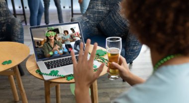 Barda elinde bira olan melez bir adam dizüstü bilgisayardaki arkadaşlarına St. Patrick 'in günü videosu için el sallıyor. İrlanda Koruyucu Azizler Günü 'nün kutlaması sırasında.