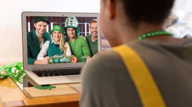 Karışık ırkçı kadın, St. Patrick 's Day videosunu evde dizüstü bilgisayarlı arkadaşlarına çekiyor. Karantina süresince evde tecrit edilmiş İrlandalı koruyucu azizlerin gününü kutluyoruz..