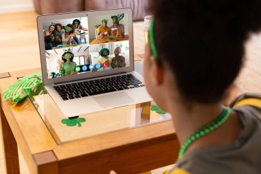 Karışık ırkçı kadın evdeki laptopta Patrick 'in günü için arkadaşlarına video görüşmesi yapıyor. Karantina süresince evde tecrit edilmiş İrlandalı koruyucu azizlerin gününü kutluyoruz..