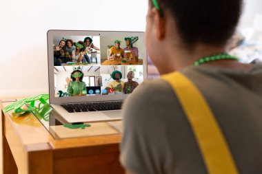 Karışık ırkçı kadın evdeki laptopta Patrick 'in günü için arkadaşlarına video görüşmesi yapıyor. Karantina süresince evde tecrit edilmiş İrlandalı koruyucu azizlerin gününü kutluyoruz..