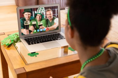 Karışık ırk kadını, St. Patrick 's Day video görüşmesini yapıyor. Evde dizüstü bilgisayardan bira içen erkek arkadaşlarıyla. Karantina süresince evde tecrit edilmiş İrlandalı koruyucu azizlerin gününü kutluyoruz..