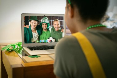 St. Patrick Günü 'nde laptopta üç erkek arkadaşıyla video görüşmesi yapan melez bir kadın. Karantina süresince evde tecrit edilmiş İrlandalı koruyucu azizlerin gününü kutluyoruz..