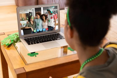 St. Patrick Günü 'nde laptopta bir grup arkadaşıyla video görüşmesi yapan melez bir kadın. Karantina süresince evde tecrit edilmiş İrlandalı koruyucu azizlerin gününü kutluyoruz..