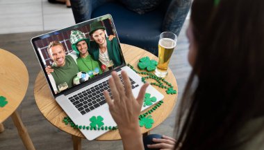 Bardaki beyaz kadın dizüstü bilgisayardaki kostümlü arkadaşlarına Aziz Patrick günü videosu çekiyor. İrlanda Koruyucu Azizler Günü 'nün kutlaması sırasında.