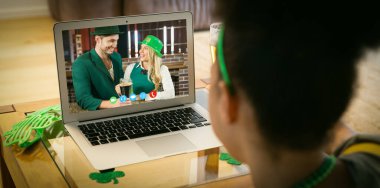 Karışık ırk kadını, St. Patrick 'in evinde dizüstü bilgisayarda kostümlü çifti videoya çekiyor. Karantina süresince evde tecrit edilmiş İrlandalı koruyucu azizlerin gününü kutluyoruz..