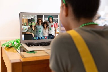 Karışık ırkçı kadın evdeki dizüstü bilgisayardaki çeşitli grup arkadaşlarına Aziz Patrick Günü videosu çekiyor. Karantina süresince evde tecrit edilmiş İrlandalı koruyucu azizlerin gününü kutluyoruz..