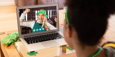 Karışık ırk kadını, dizüstü bilgisayarında Aziz Patrick Günü videosu ile mutlu bir bayan arkadaşı arıyor. Karantina süresince evde tecrit edilmiş İrlandalı koruyucu azizlerin gününü kutluyoruz..