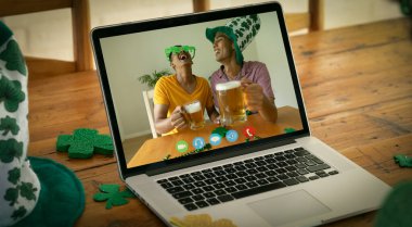 İki karışık ırkçı erkek arkadaş ve bira evde dizüstü bilgisayarla Aziz Patrick Günü 'nü videoya çekiyor. Karantina süresince evde tecrit edilmiş İrlandalı koruyucu azizlerin gününü kutluyoruz..