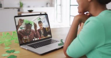 Laptoptaki görüntülü aramada, biralı, yonca şekilli şeyler giyen gülümseyen çift. İrlanda geleneği ve Aziz Patrick Günü kutlama konsepti dijital olarak oluşturulmuş video.