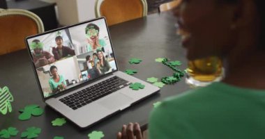 Laptop 'taki görüntülü aramada gülen, biralı, yonca şekilli eşyalar giyen bir grup arkadaş. İrlanda geleneği ve Aziz Patrick Günü kutlama konsepti dijital olarak oluşturulmuş video.