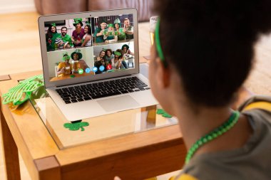 Karışık ırkçı kadın evdeki laptopta Patrick 'in günü için arkadaşlarına video görüşmesi yapıyor. Karantina süresince evde tecrit edilmiş İrlandalı koruyucu azizlerin gününü kutluyoruz..