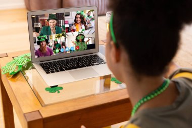 Karışık ırkçı kadın evdeki laptopta Patrick 'in günü için arkadaşlarına video görüşmesi yapıyor. Karantina süresince evde tecrit edilmiş İrlandalı koruyucu azizlerin gününü kutluyoruz..