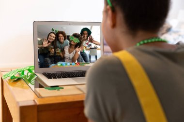 Karışık ırkçı kadın evdeki dizüstü bilgisayardaki çeşitli grup arkadaşlarına Aziz Patrick Günü videosu çekiyor. Karantina süresince evde tecrit edilmiş İrlandalı koruyucu azizlerin gününü kutluyoruz..