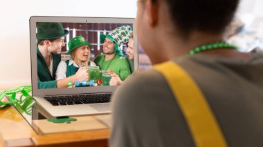 Karışık ırkçı kadın, St. Patrick 's Day videosunu evde dizüstü bilgisayarında kostüm giymiş bir grup arkadaşına çekiyor. Karantina süresince evde tecrit edilmiş İrlandalı koruyucu azizlerin gününü kutluyoruz..