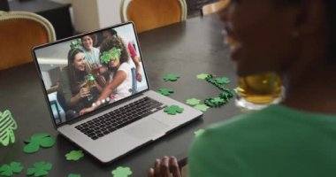 Laptop 'taki görüntülü aramada gülen, biralı, yonca şekilli eşyalar giyen bir grup arkadaş. İrlanda geleneği ve Aziz Patrick Günü kutlama konsepti dijital olarak oluşturulmuş video.