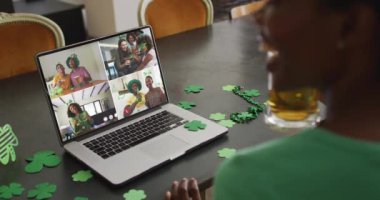 Laptop 'taki görüntülü aramada gülen, biralı, yonca şekilli eşyalar giyen bir grup arkadaş. İrlanda geleneği ve Aziz Patrick Günü kutlama konsepti dijital olarak oluşturulmuş video.