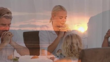 Yemekten önce birlikte dua eden çok nesilli beyaz bir ailenin günbatımının animasyonu. din, inanç ve Hıristiyanlık kavramı dijital olarak oluşturulmuş video.