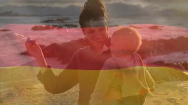 Almanya bayrağının mutlu Kafkasyalı anne üzerinde canlandırılması ve çocuğun sahilde köpük üflemesi. Vatanseverlik ve kutlama konsepti dijital olarak oluşturulmuş video.