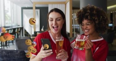 Birayla akıllı telefon kullanan mutlu bayan arkadaşlar yerine emoji simgelerinin animasyonu. Sosyal medya ve iletişim arayüzü kavramı dijital olarak oluşturulmuş video.