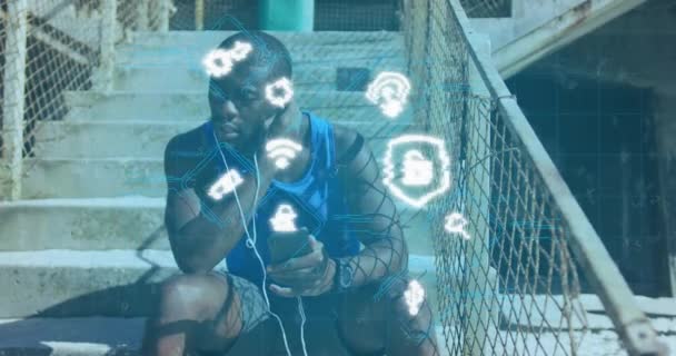 アフリカ系アメリカ人男性がイヤフォンを屋外で身に着けているメディアアイコンのアニメーション 健康とフィットネスの概念をデジタルで生成し — ストック動画