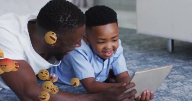 Mutlu Afro-Amerikan baba ve oğlunun tablet kullanması üzerine duygu simgelerinin animasyonu. aile, birliktelik, teknoloji konseptiyle dijital olarak oluşturulmuş video ile zaman geçirme.