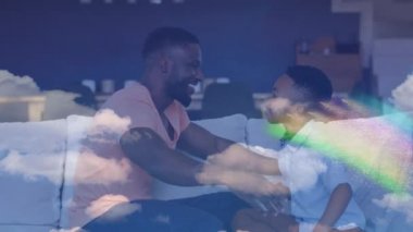 Mutlu Afro-Amerikan baba ve oğlunun kanepede kucaklaşması üzerine gökkuşağı animasyonu. aile, birliktelik, kaliteli zaman konsepti dijital olarak oluşturulmuş video.