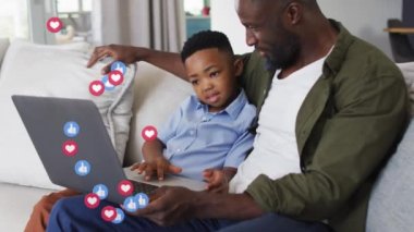 Mutlu Afro-Amerikan baba ve oğlunun dizüstü bilgisayar kullanması üzerine duygu simgelerinin animasyonu. aile, birliktelik, kaliteli zaman konsepti dijital olarak oluşturulmuş video.